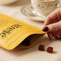 A yellow stand-up pouch of xtreSé Hair Growth Gummies with two red gummies placed with hand model at skin type solutions